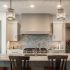 A clean kitchen with an island and bar stools, sparkling light fixtures overhead