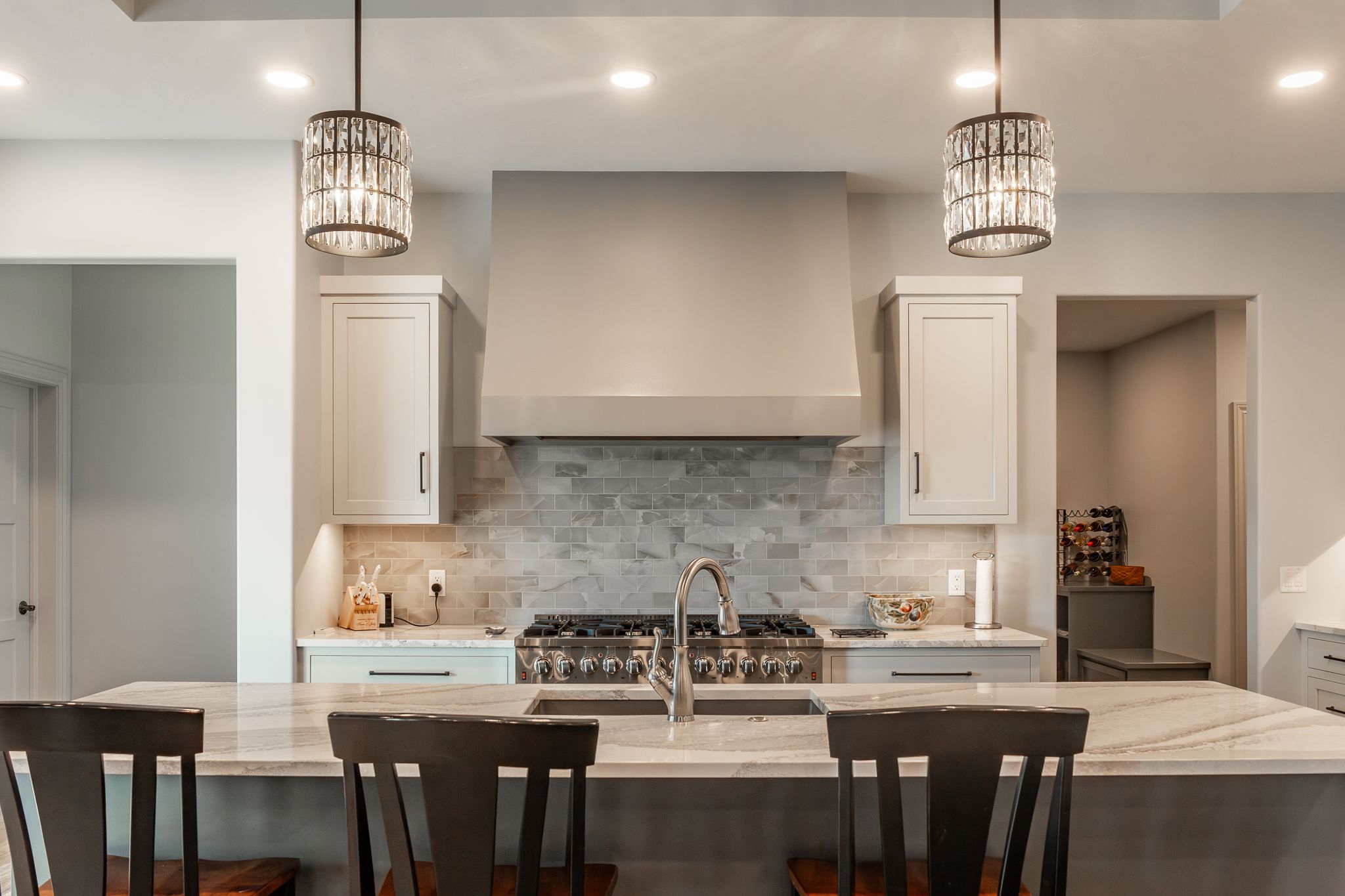 A clean kitchen with an island and bar stools, sparkling light fixtures overhead