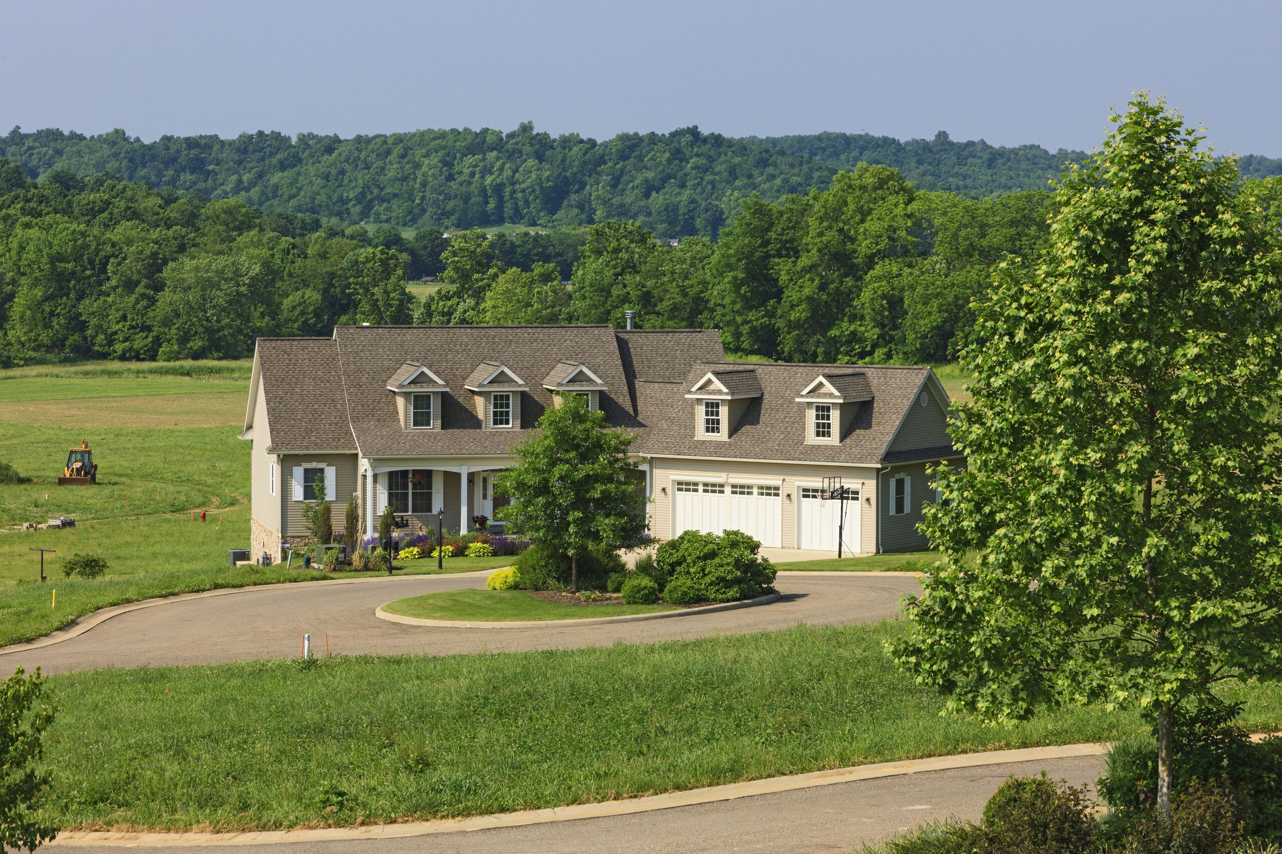 View of custom luxury home surrounded by trees and pasture